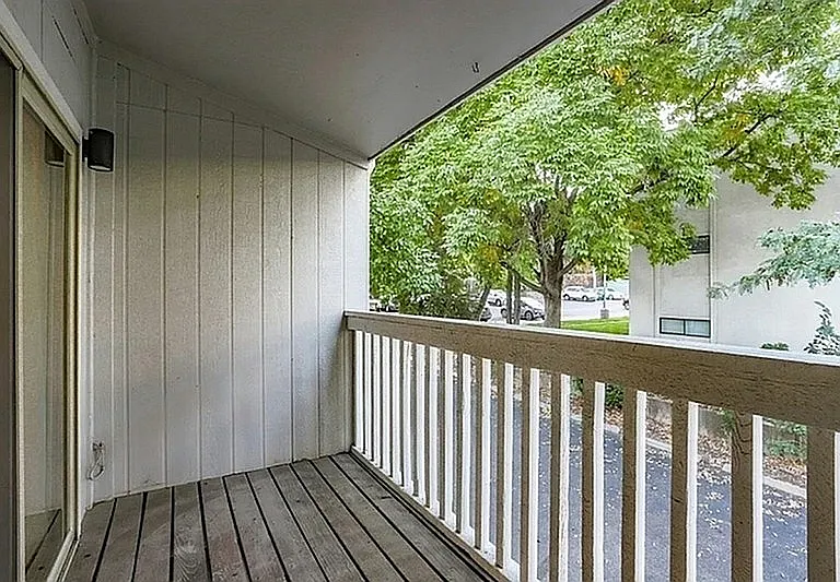 Charming apartment balcony with wooden decking and tranquil views of lush green trees, perfect for serene outdoor relaxation.