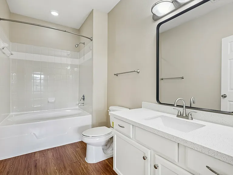 Elegant bathroom with modern fixtures, featuring a large mirror, pristine white counter, spacious bathtub, and sleek wood-style flooring. Elegant bathroom with modern fixtures, featuring a large mirror, pristine white counter, spacious bathtub, and sleek