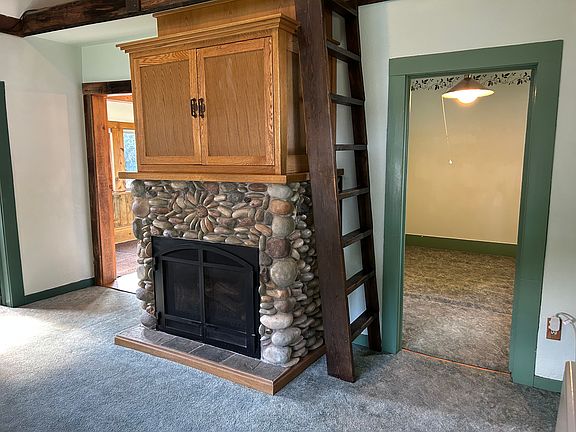 Propane fireplace, ladder to upstairs loft and view into bedroom. Cabinet above fireplace has shelves for stereo components and a mount for a flat screen TV.