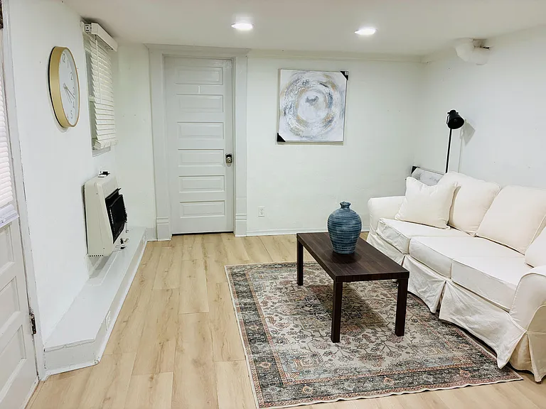 Shared living area with comfortable seating, coffee table, and wood-look flooring, plus window blinds and ceiling lighting.