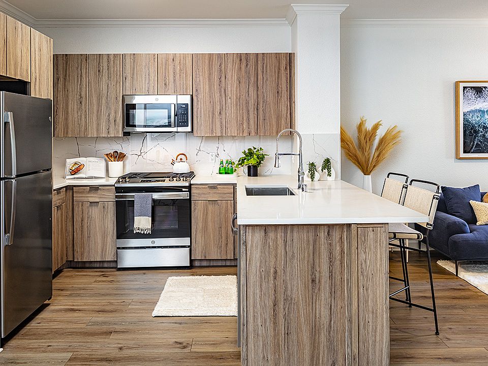 Apartment kitchen with stainless steel appliances, quartz countertops and wood-style flooring.