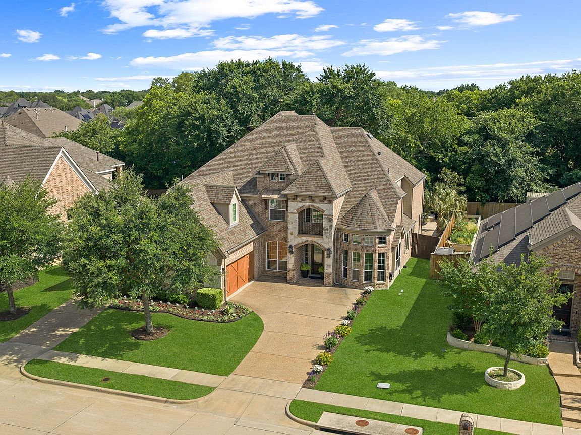 Front elevation of 8609 Tuscan Oaks Drive in McKinney, Texas — a two-story brick and stone estate with arched entry, manicured lawn, and three-car front-entry garage