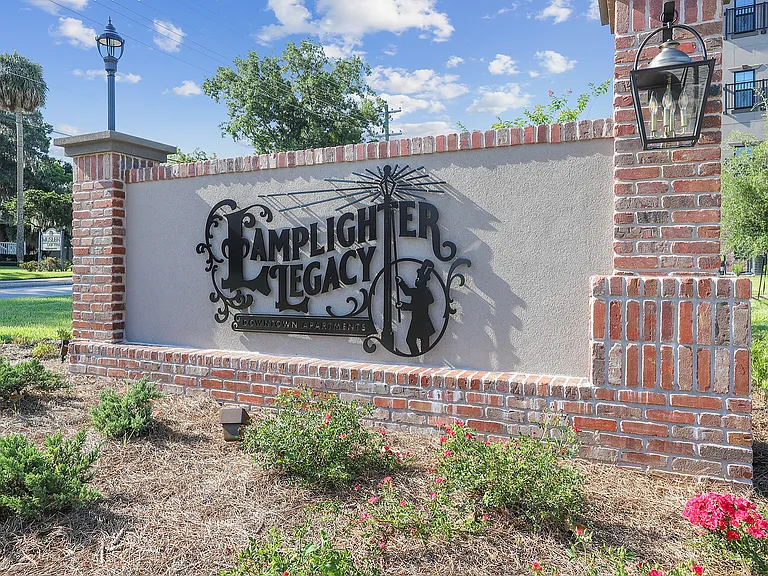 Inviting Lamplighter Legacy sign with vintage lamppost design, surrounded by lush greenery and vibrant flowers in a charming setting.