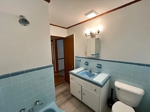 Vintage-inspired bathroom featuring original powder blue ceramic tile matching retro bathtub with coordination built-in since surround. The space offers a clean, well-maintained aesthetic with updated LVP flooring, natural light from large window, and a c
