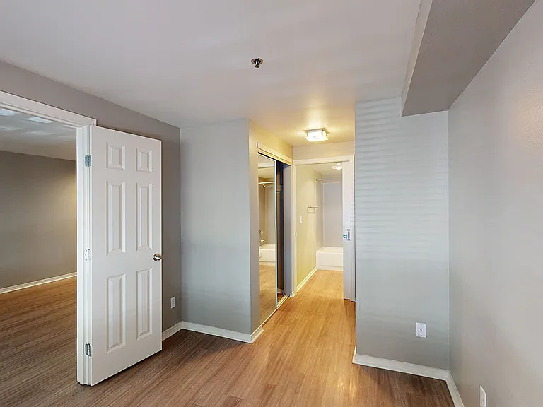 Spacious apartment bedroom with attached bathroom and wood-style flooring.