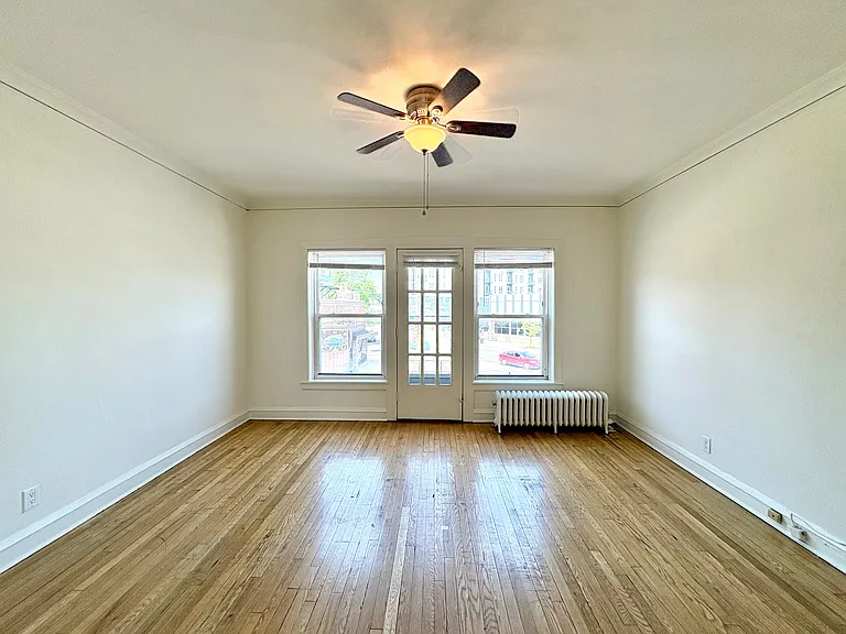 Bright and spacious living room with polished hardwood floors, large windows, and a ceiling fan, offering cozy urban views. Bright and spacious living room with polished hardwood floors, large windows, and a ceiling fan, offering cozy urban views.