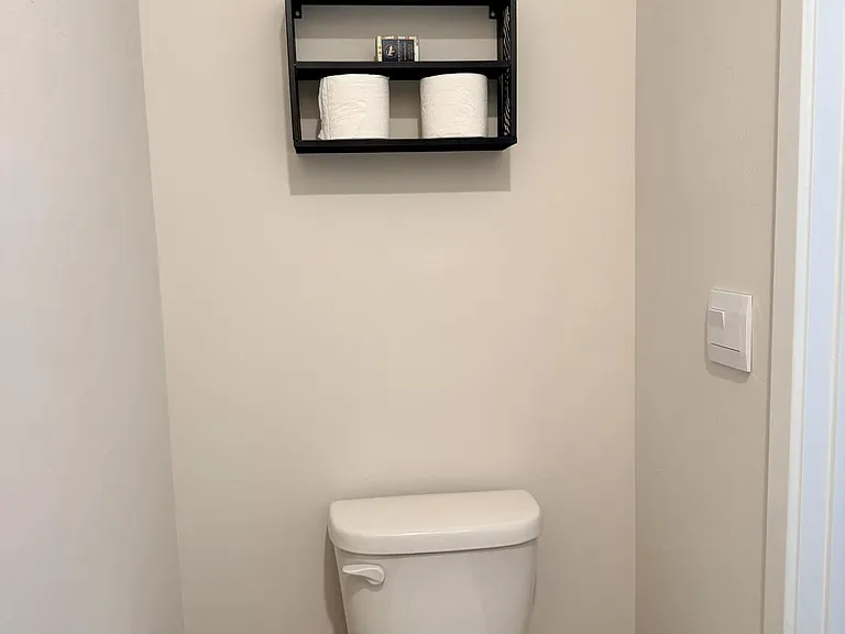 Neat bathroom nook with a standard toilet, floating wall shelf for essentials, and easy-care flooring for simple upkeep.