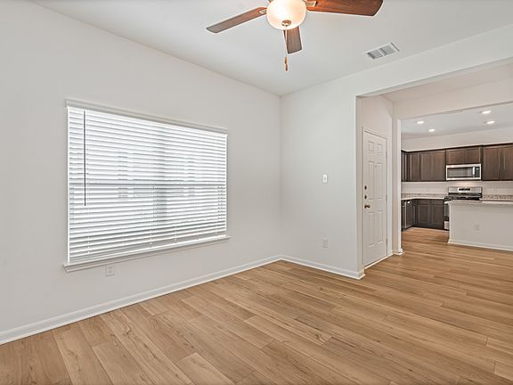 Spacious family room with wood-style flooring, large windows, and a ceiling fan.