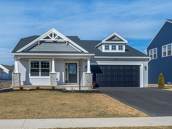 Straight-on view of the homes front elevation featuring a covered porch, stone columns, and dark gar
