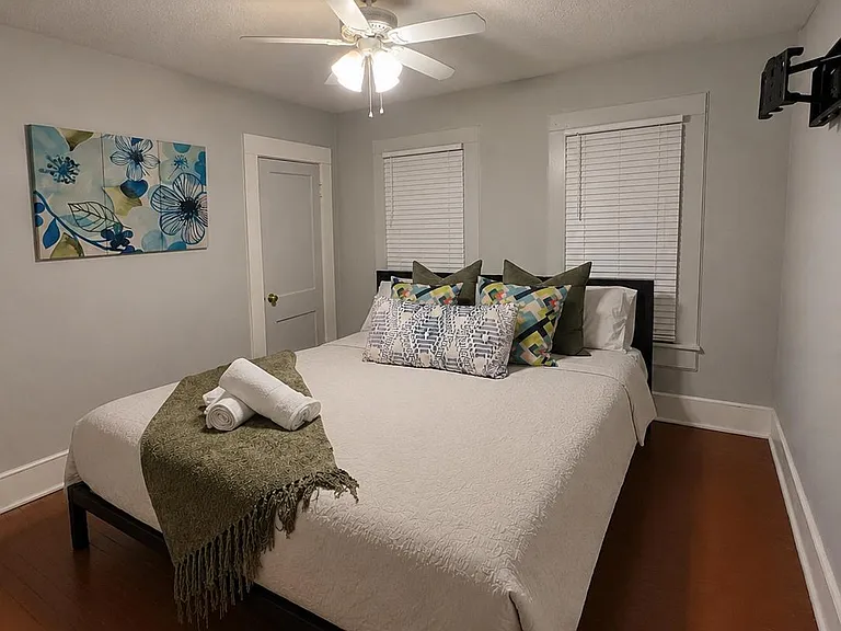 Furnished bedroom with hardwood floors, ceiling fan, and two windows with blinds for privacy and natural light.