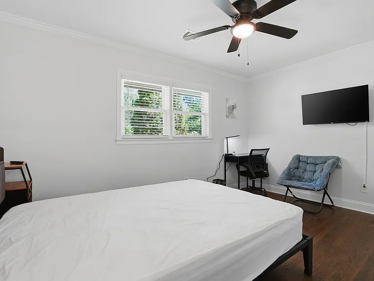Private bedroom with large window, ceiling fan, wall-mounted TV, and a dedicated desk area for work or study.