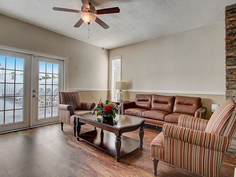 Inviting living room with elegant hardwood floors, plush leather sofa, striped armchairs, and bright natural light from double glass doors.