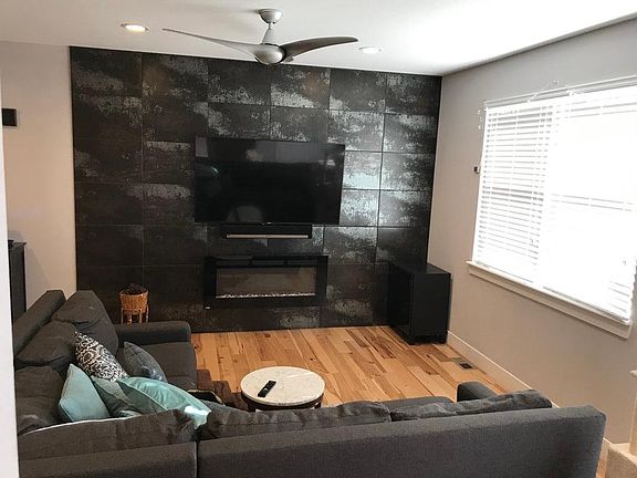 Family room with elegant Italian tile features electric fireplace, TV wall mount & ceiling fan.