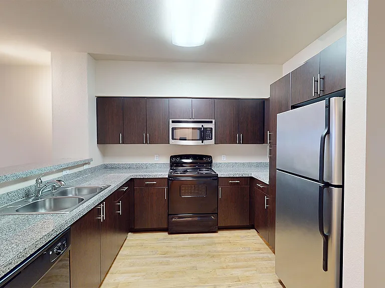 Apartment kitchen with granite countertops and wood-style flooring.