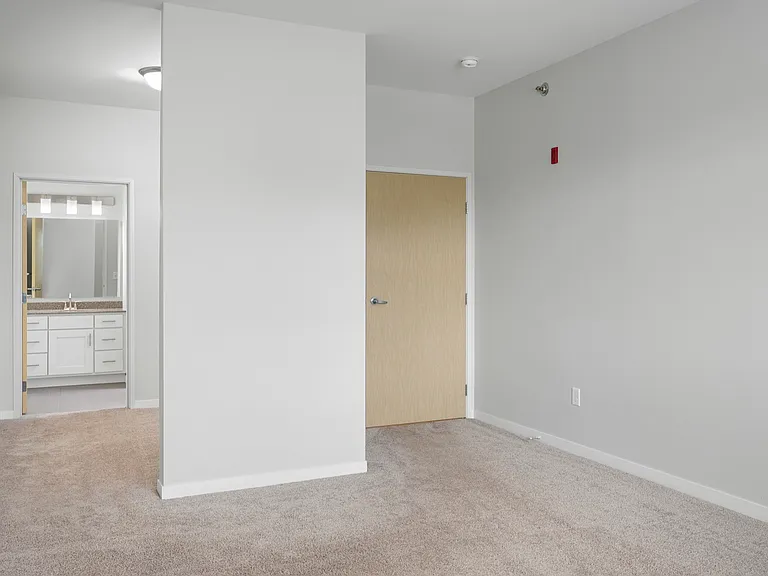 Bright and cozy apartment interior with plush carpeting, neutral walls, and a view into a modern bathroom featuring ample storage with white cabinets. Bright and cozy apartment interior with plush carpeting, neutral walls, and a view into a modern bathroo