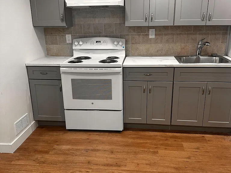Kitchen features ample cabinet storage, tiled backsplash, durable countertops, and an electric range with vent hood.