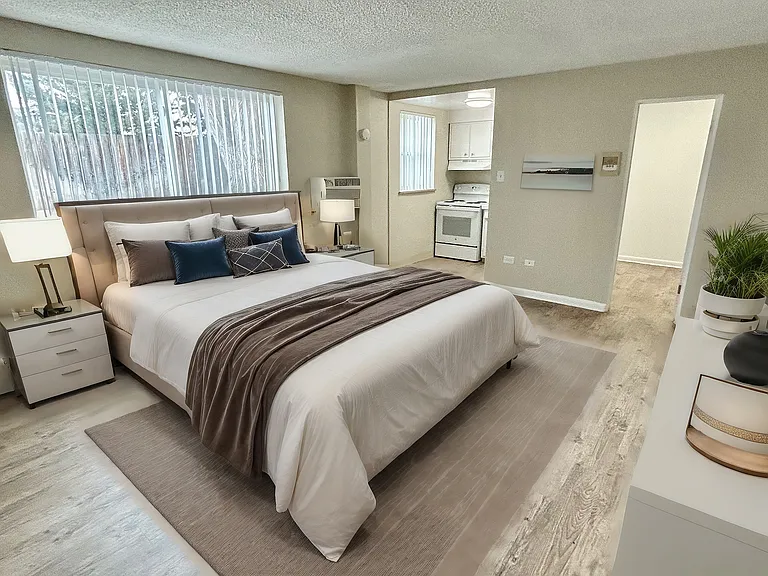 Inviting bedroom with elegant decor, featuring a plush bed, stylish bedside lamps, and a glimpse into a cozy kitchen.