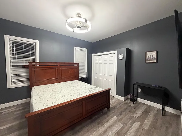 Spacious bedroom with a queen bed, durable flooring, and two windows with blinds for privacy and daylight.