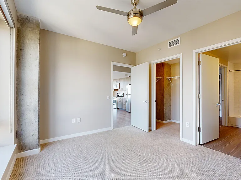 Spacious apartment bedroom with large closet, attached bathroom and plush carpet flooring.