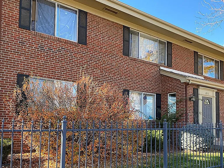 Charming two-story brick building with large windows and manicured bushes, ideal for cozy living.