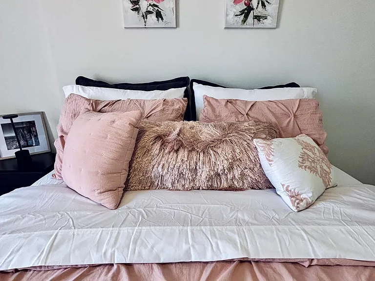 Comfortable bedroom featuring a neatly made bed with layered linens, decorative wall art, and a bedside table for essentials.