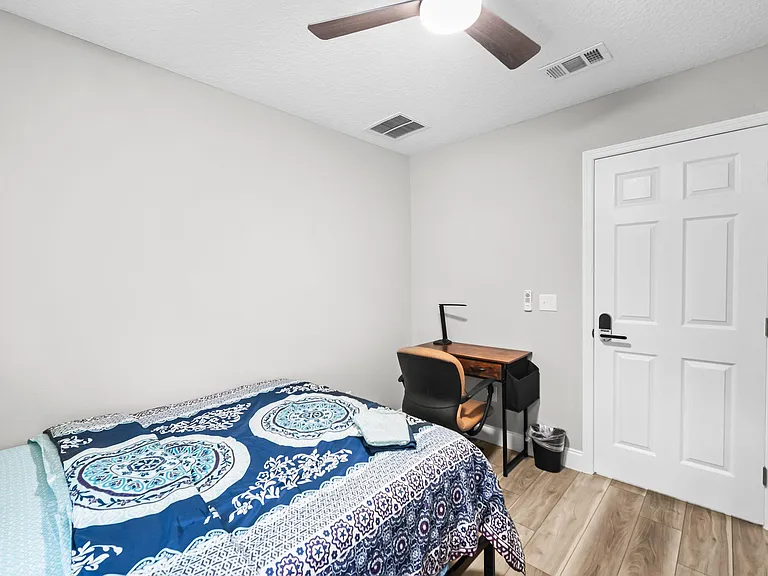 Furnished bedroom with ceiling fan, wood-style flooring, and a dedicated desk workspace for studying or remote work.