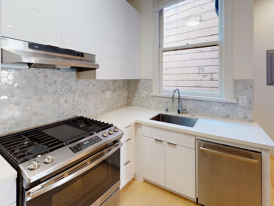 Modern kitchen featuring stainless steel appliances, cabinetry, hexagonal tile backsplash, and plenty of natural light.