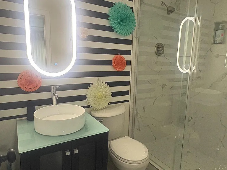 Stylish bathroom with glass-enclosed shower, marble-look tile, vessel sink vanity, and illuminated mirror.