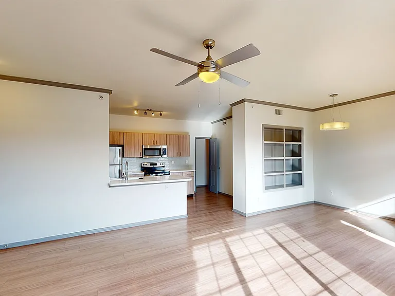 Apartment kitchen with stainless steel appliances, dining and living room with wood-style flooring.