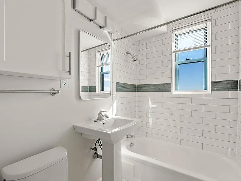 Bright and airy bathroom featuring modern white subway tiles, with a glass tile accent, a sleek pedestal sink, cabinetry for toiletries, and natural light