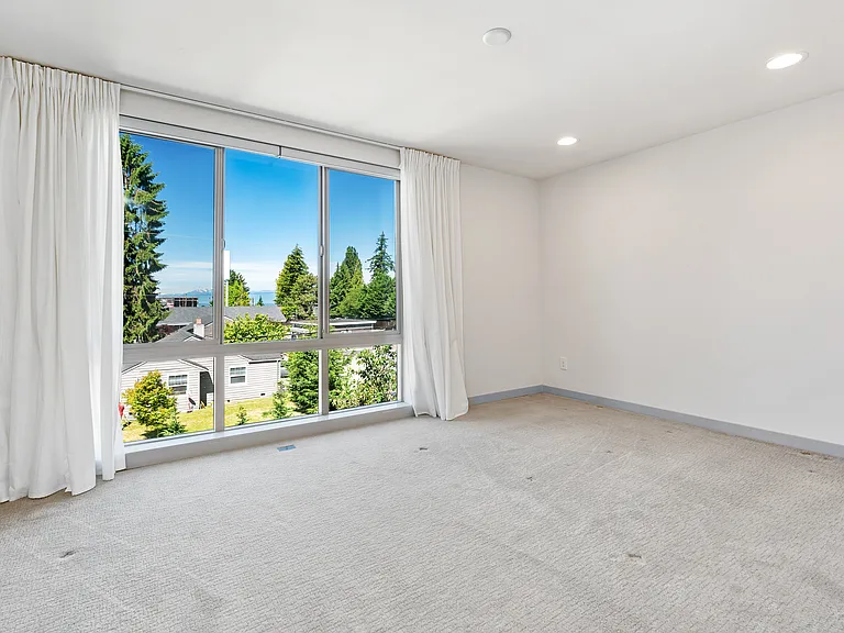 Sunshine drenched primary suite with floor-to-ceiling windows, curtains and automatic blinds.