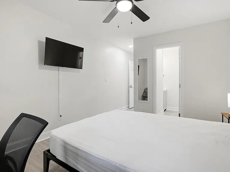 Private bedroom with a ceiling fan, wall-mounted TV, and convenient bedside table lighting near the entry/closet area.
