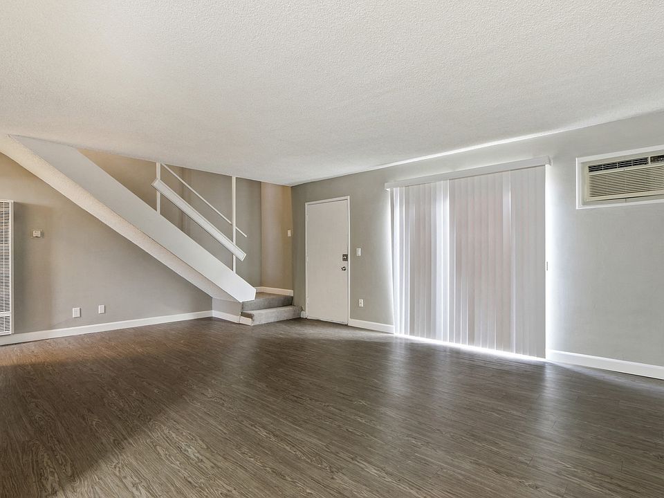 Living room with air conditioning on the right, wood-style flooring, vertical blinds, carpeted staircase to the second floor