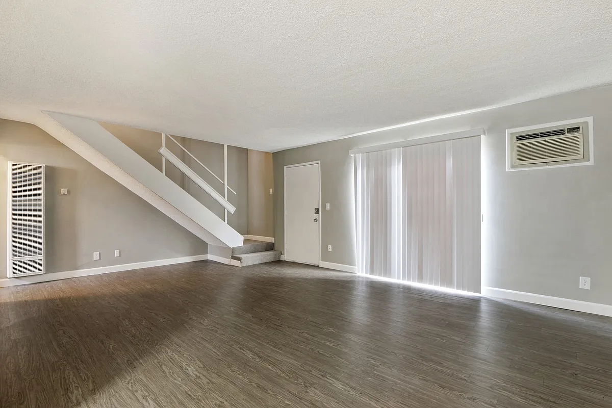 Living room with air conditioning on the right, wood-style flooring, vertical blinds, carpeted staircase to the second floor - 620 S Lemar Park Dr
