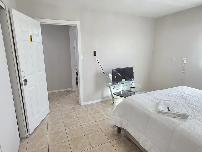 Private bedroom with tiled flooring, neutral walls, and space for a bed plus a small desk/TV setup.