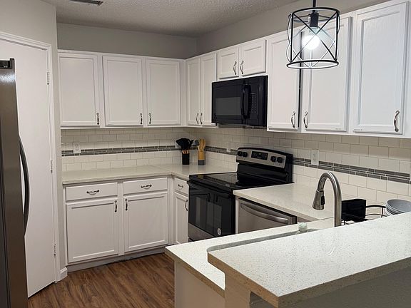 Updated kitchen with ample white cabinetry, subway-tile backsplash, and a breakfast bar plus black appliance package.