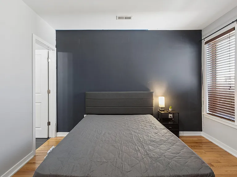 Private bedroom with hardwood floors, a comfortable bed setup, and a large window with blinds for light control.