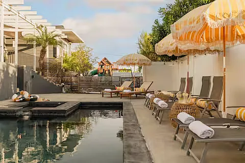 Resort-style outdoor space with a heated pool, hot tub, sun loungers with umbrellas, and cozy seating. Perfect for relaxing, sunbathing, or enjoying poolside drinks, this stylish area offers a luxurious retreat for ultimate leisure.