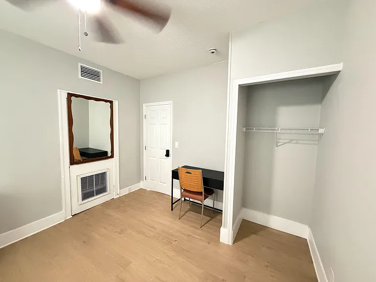 Neat bedroom nook with a built-in closet, hardwood-style floors, and a compact desk setup for work or study.