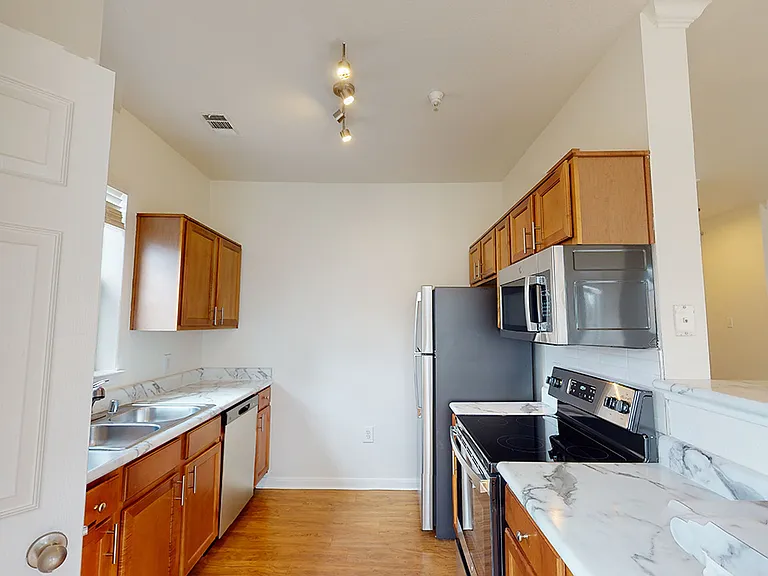Apartment kitchen with stainless steel appliances, wood-style flooring, and marble-style countertops (shown here). Quartz-style countertops are available in select homes.