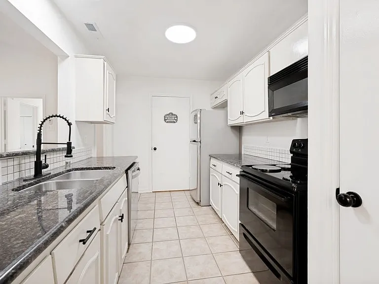 Galley kitchen featuring white cabinetry with dark hardware, granite countertops, a subway tile backsplash, and ceramic tile flooring