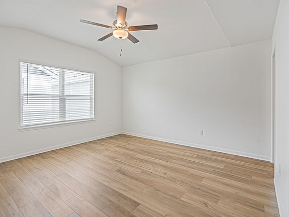 Master bedroom with a vaulted ceiling, tan carpet, and a large window.