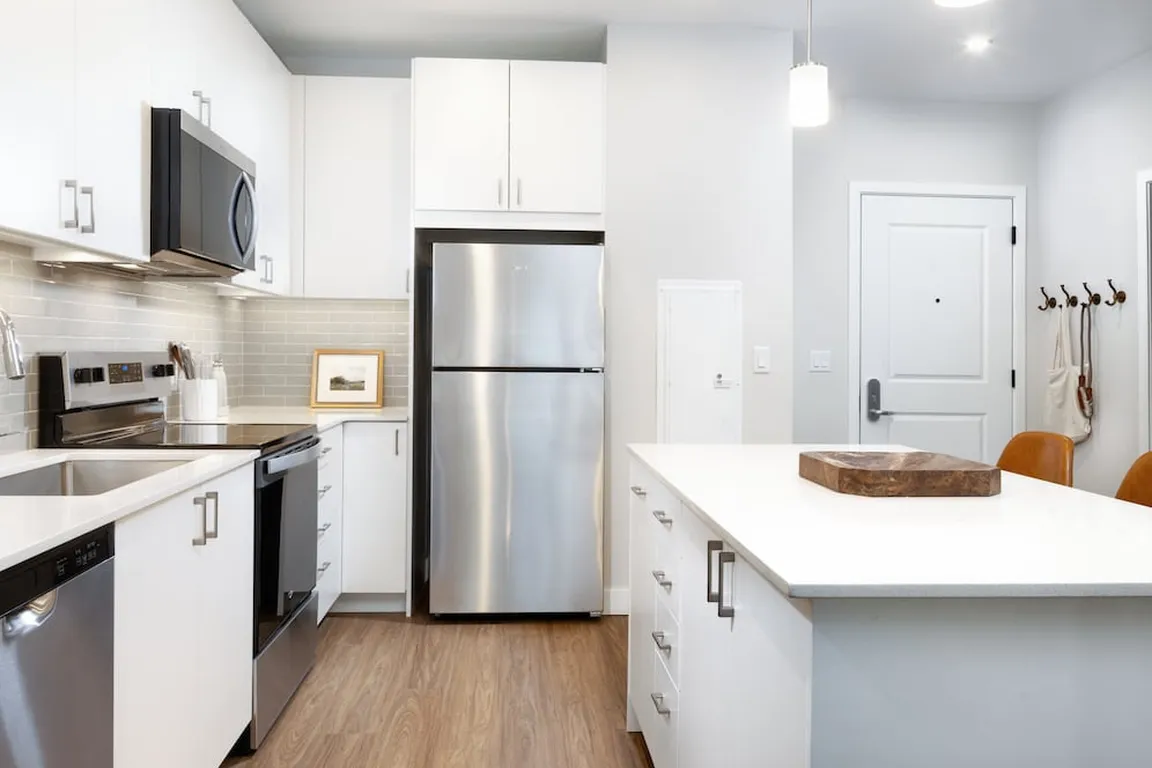 Design Collection I kitchen with stainless steel appliances, white cabinetry, grey tile backsplash, under-cabinet lighting, white quartz countertops, and hard surface flooring