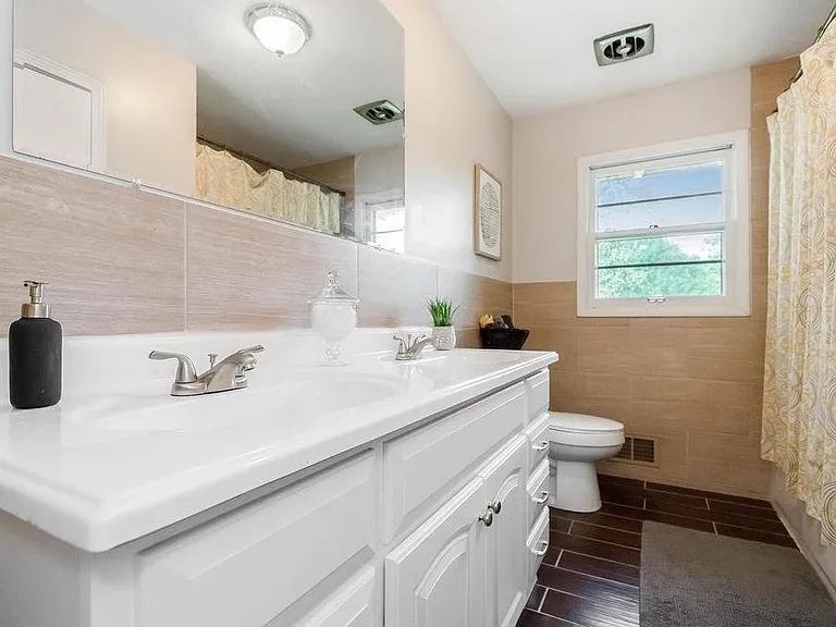 Bathroom with double-sink vanity, wide mirror, and a tub/shower combo beside a window for ventilation and light.
