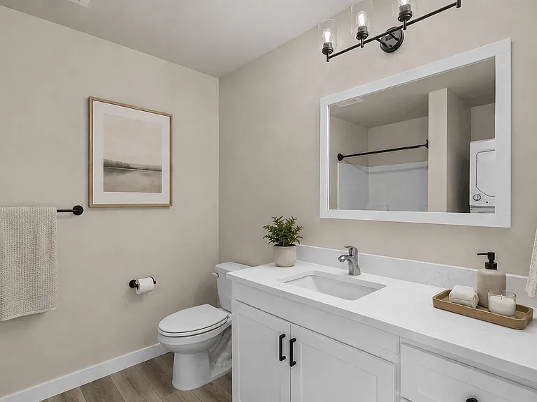 Modern apartment bathroom with quartz vanity, framed mirror, contemporary lighting, decorative artwork, and stylish staging accents. Modern apartment bathroom with quartz vanity, framed mirror, contemporary lighting, decorative artwork, and stylish stagin