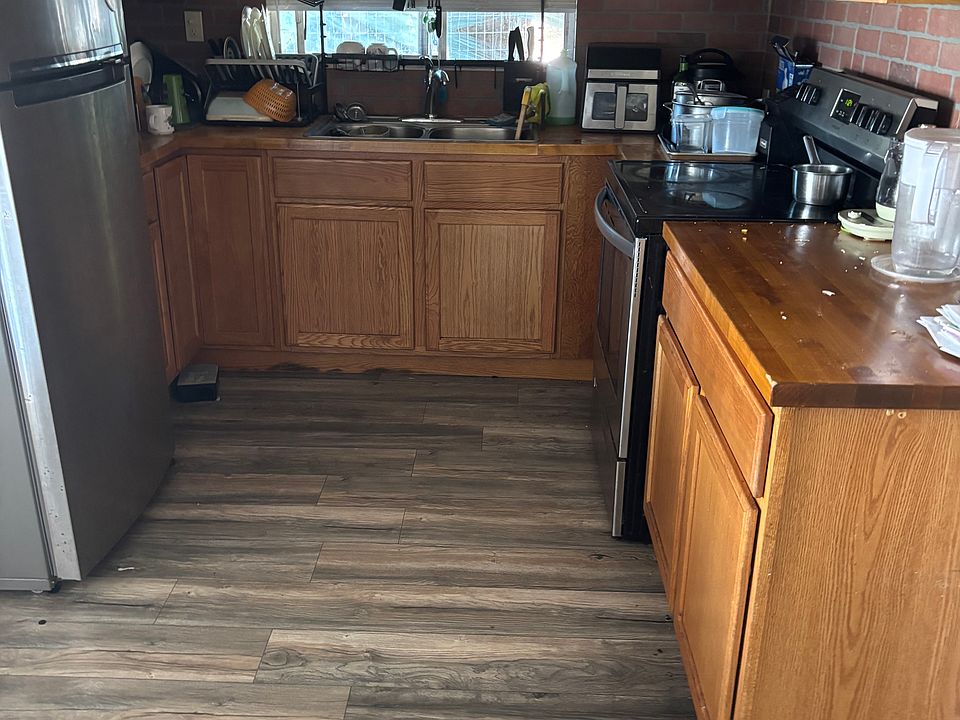 Bright kitchen featuring warm wood cabinetry, stainless steel refrigerator and oven, a large window above the sink for natural light, and durable gray slate wood-look flooring