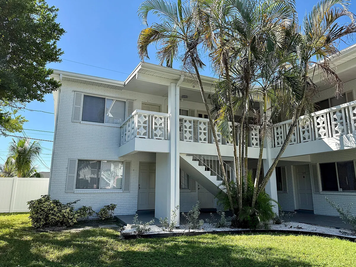 Charming two-story apartment building with white brick exterior, lush palm trees, and inviting balconies under a clear blue sky. - Palms on 31st