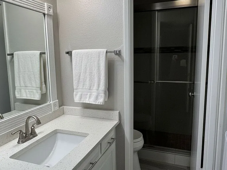 Chick and Stylish | The first bathroom with a modern design shower with cool sliding doors, and toilet, separate from your quartz-top sink. Your in-unit new LG washer and dryer tucked conveniently in the niche across your sink and cabinets.