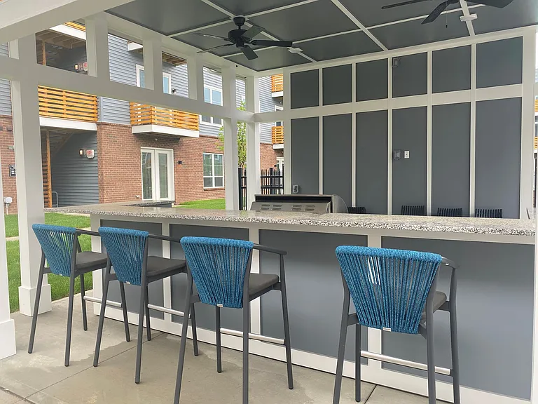 Standing in front of the grilling station. There is a granite bar with 4 bar stools. Behind the bar is a propane grill for the community.
