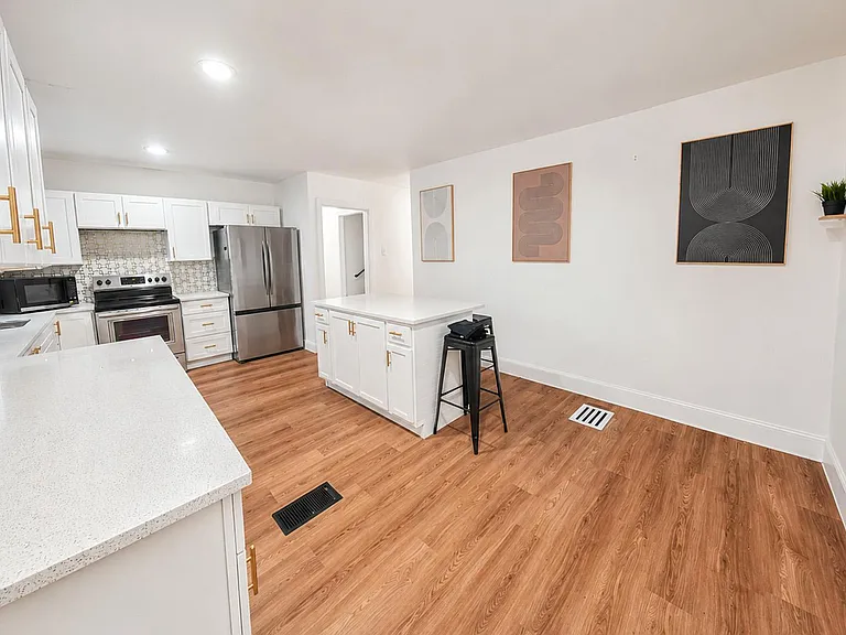 Spacious kitchen with white cabinetry, quartz-style counters, center island seating, and stainless steel appliances.